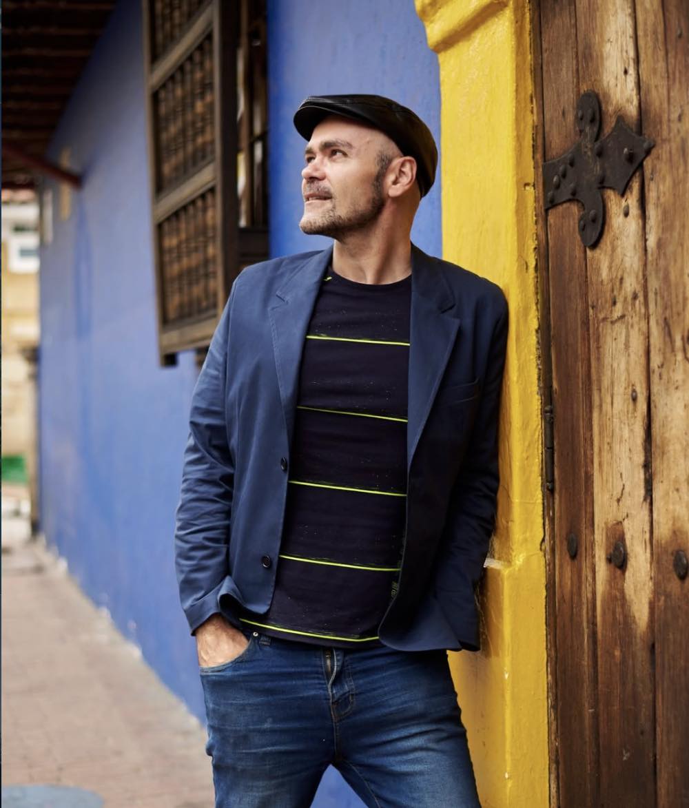 Fabrice Dubesset avec un chapeau, devant une façade colorée